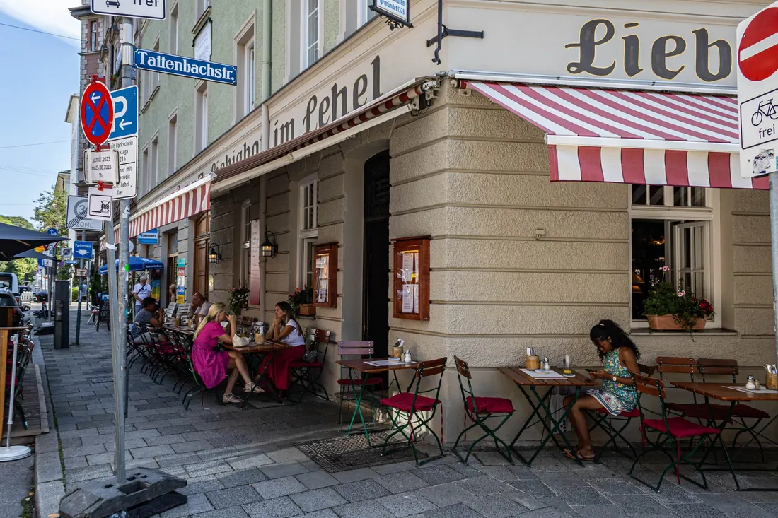 Gäste sitzen an einem Sommertag draußen vor dem Liebighof, unter der rot-weißen Markise an der Ecke Liebigstraße/Tattenbachstraße